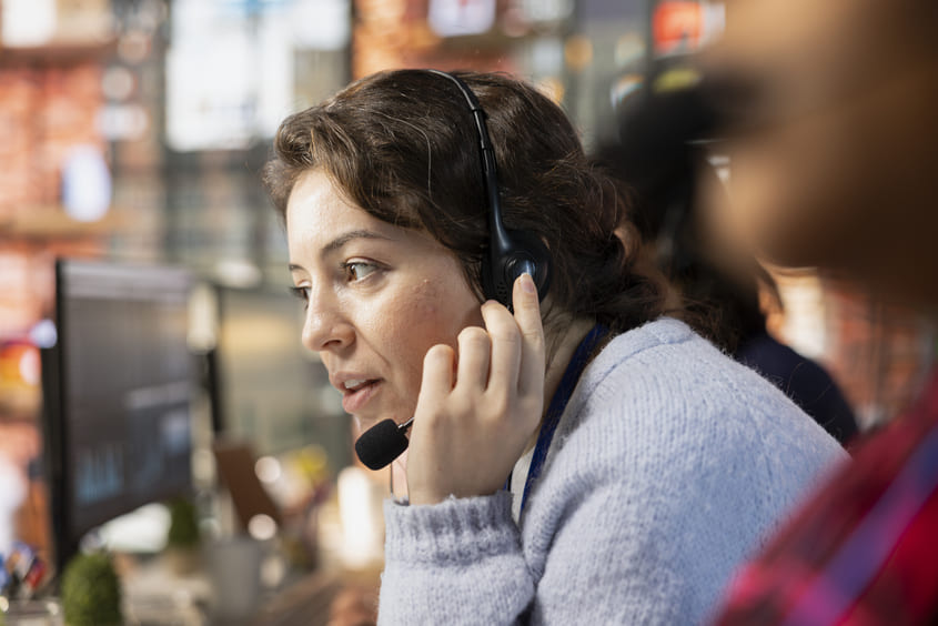 Mulher usando headset presta atendimento ao cliente em ambiente de call center.