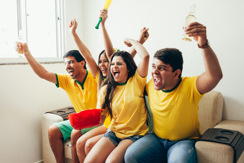Group of friends watching soccer game on television, celebrating goal and screaming